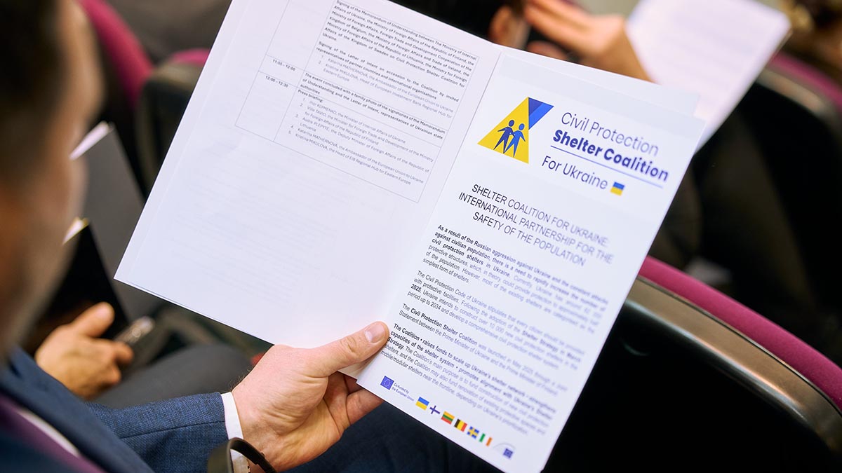 A man is sitting in the stands and looking at a brochure from the civil protection coalition that he is holding in his hand.