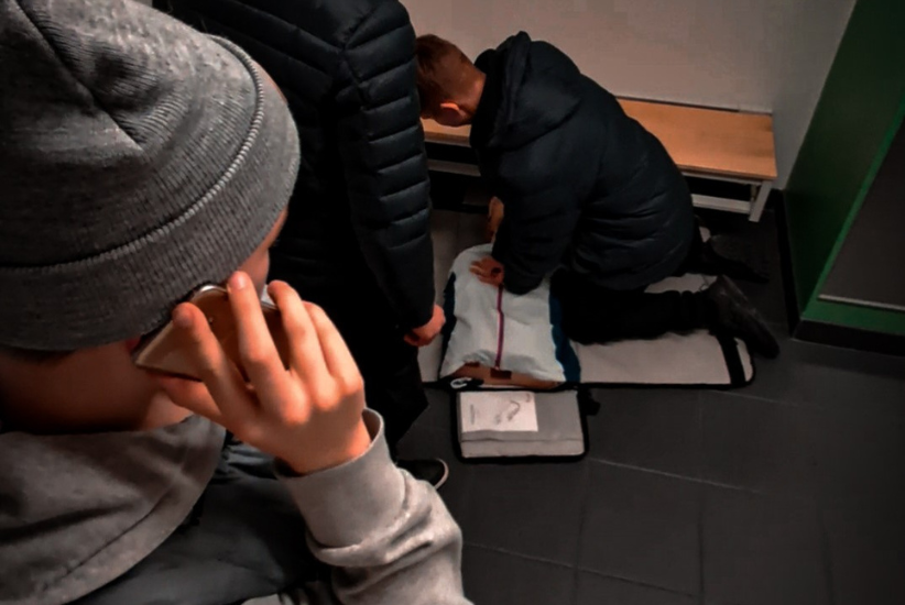 Nuori soittaa puhelimeen, taustalla harjoitellaan elvytystä.