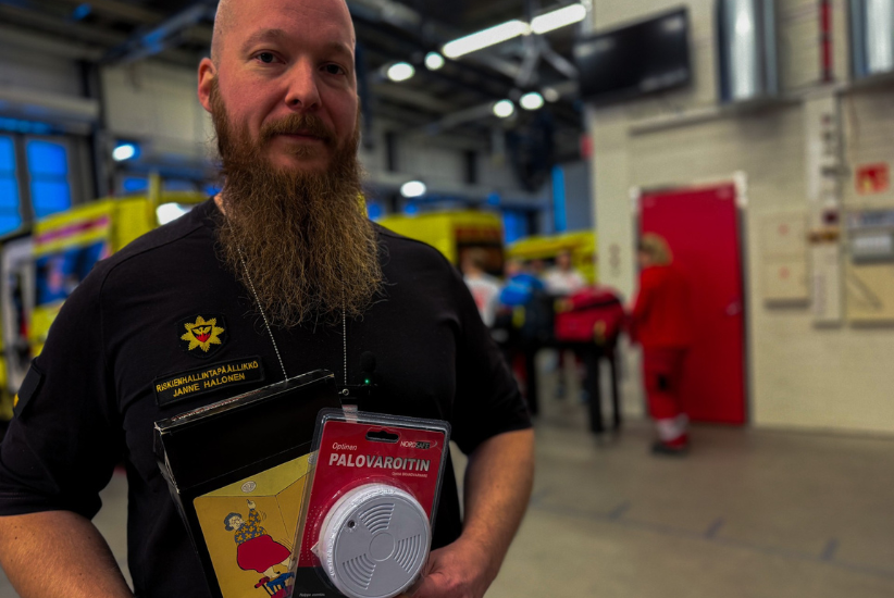 Henkilö seisoo pelastusaseman kalustohallissa ja pitelee palovaroitinta käsissään.