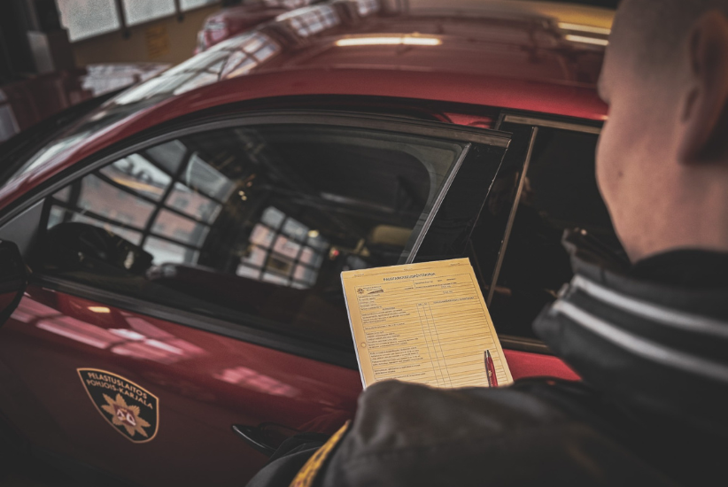 Pelastusviranomainen pitelee kädessään palotarkastuksen pöytäkirjaa, auto taustalla.