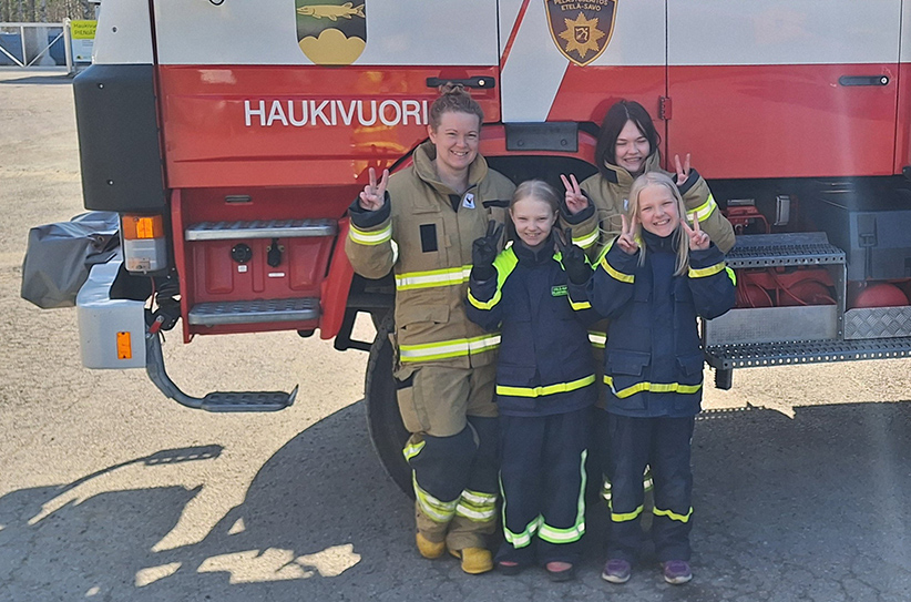 Mira Pieviläinen ja hänen tyttärensä hymyilevät ja näyttävät voiton merkkejä Haukivuoren paloauton vieressä.