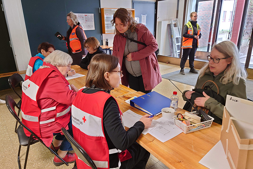 Kuvituskuva häiriötilannekeskuksen kirjauspisteeltä, jossa Punaisen ristin työntekijät kirjaavat keskukseen tulijat sisään.