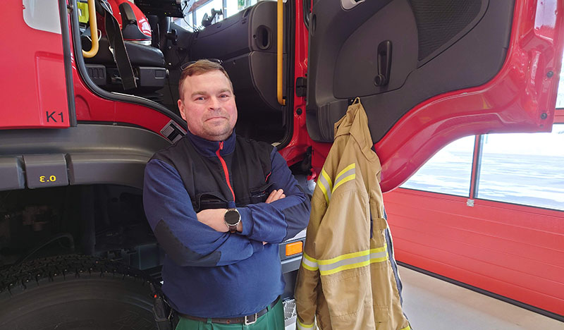 Ismo Pirskanen seisoo hymyillen sammutusauton edessä.