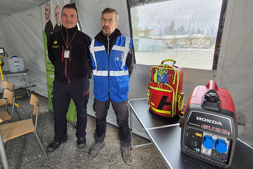 Riskienhallintapäällikkö Jani Jämsä Etelä-Savon pelastuslaitokselta seisoo Suur-Savon Reservilälispiirin Hannu Penttilän rinnalla. Heidän vierellään pöydällä on reserviläisten kalustoa, ensiapulaukku ja aggregaatti.