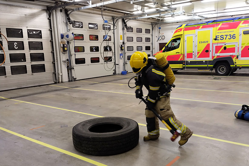 kuvituskuva: sammutusasuinen sopimuspelastaja suorittaa kuntotestiä, jossa lyödään isoa kuorma-auton rengasta lekalla.