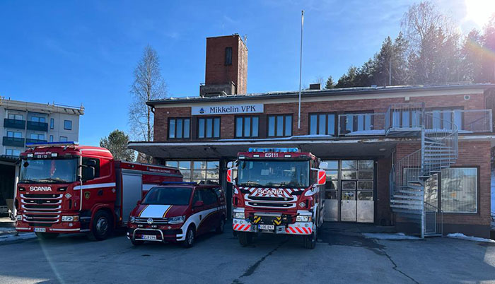  Mikkelin VPK:n punatiilinen paloasema. Aseman edustalla on pelastuskalustoa ja taustalla näkyy letkutorni. 