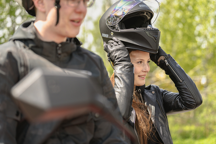 Kuvituskuvassa nuori nainen on laittamassa moottoripyöräkypärää päähänsä.