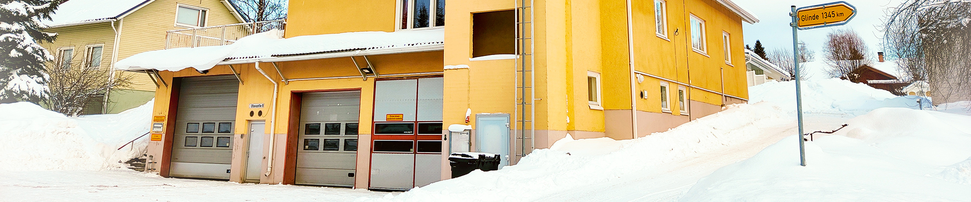 Otavan keltaiseksi maalattu paloasema sijaitsee rinteessä. Etualalla kalustohallin puoli isoine ovineen.