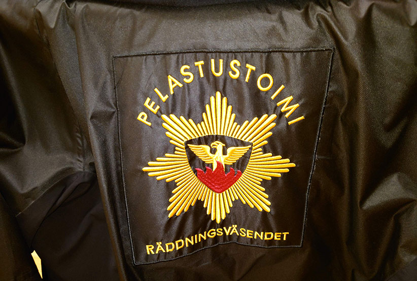 Pelastustoimen logo takin selkämyksessä.
