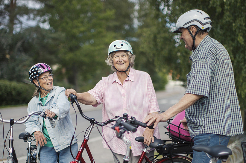 Kuvituskuvassa vähän iäkkäämpiä henkilöitä pysähtyneenä juttelemaan pyöriensä vierelle. Kaikilla on pyöräilykypärät päässä.