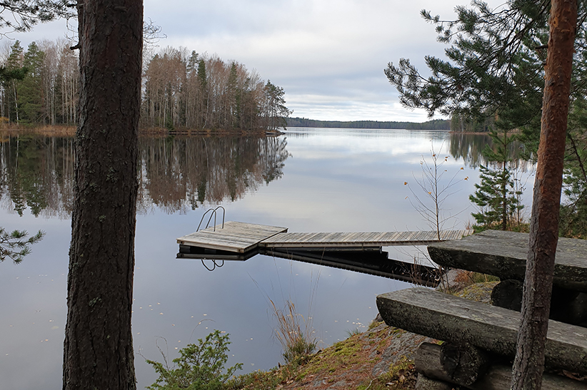 Kuvituskuva kallioisesta järvenrannasta, jossa kalliolta viettää puinen laituri järveen.