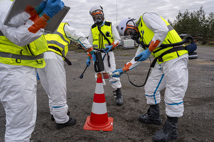 Suoja-asuihin pukeutuneet pelastustoimen asiantuntijat harjoittelevat säteilymittarin käyttöä.