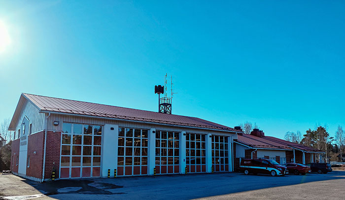  Ristiinan paloasema, jossa etualalla on kalustohalli korkeine lasiruutuisine ovineen ja taaempana toimistotilat. Rakennuksen edessä on kaksi pelastuslaitoksen autoa. 