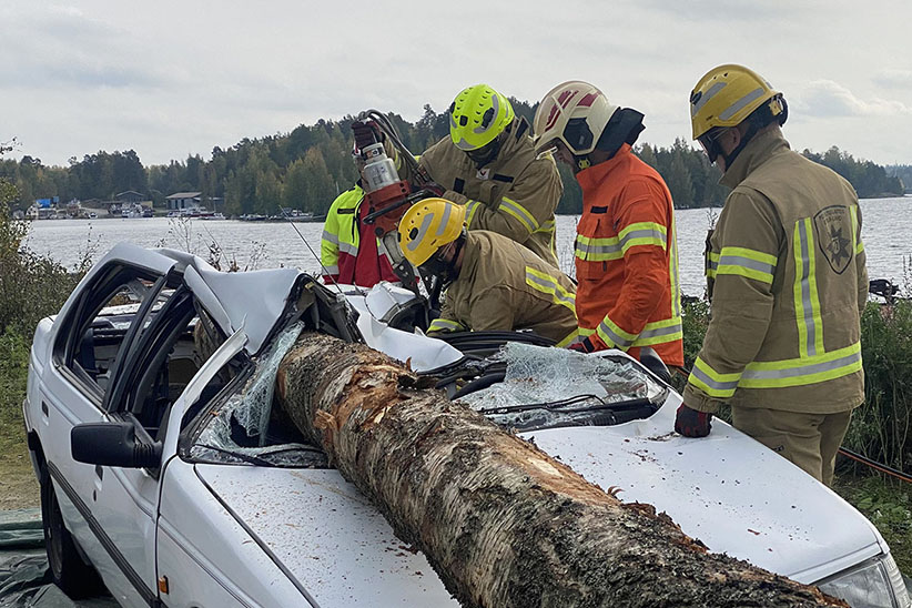 Pelastuslaitoksen ja UPM:n yhteisessä harjoituksessa puu on pudonnut kuormasta auton päälle ja pelastajat irroittavat sitä leikkurilla.