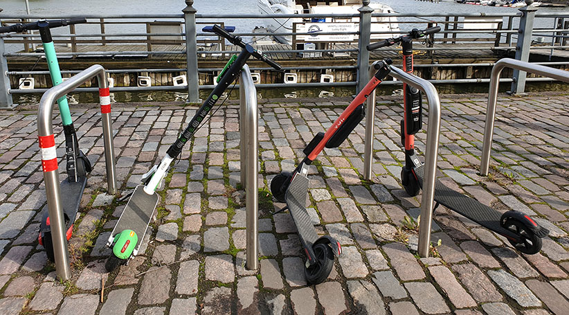 Sähköpotkulautoja parkkeerattuna telineisiin.