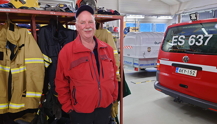  Virtasalmen sopimuspalokuntalainen Jari Hänninen seisoo sopimushenkilöstön varustehyllyn vieressä. Taaempana on palokunnan kalustoa. 