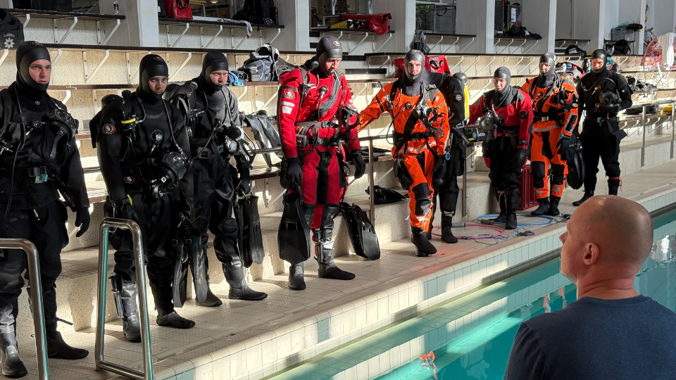 Henkilöitä sukelluspuvuissa uima-altaan reunalla