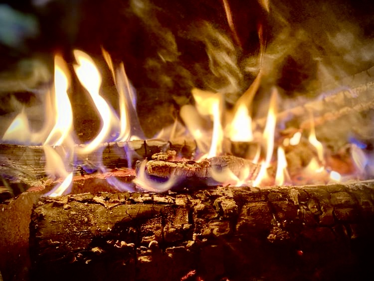 Kuva tulisijasta, jossa palaa puita.