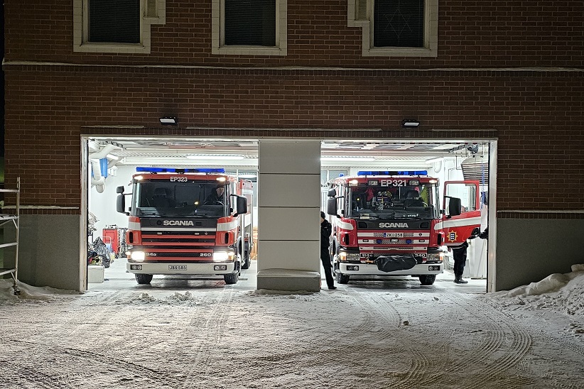 Kaksi paloautoa palotallissa, ulkona lunta.