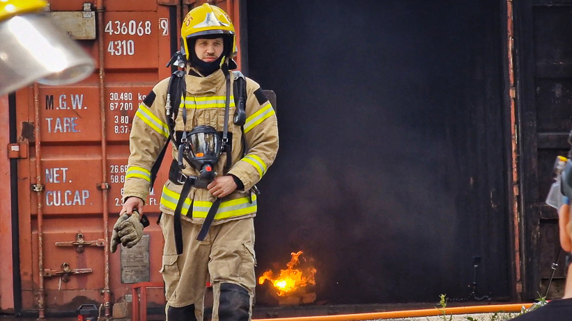 En brandman går mot kameran, ett elsparkcykelbatteri brinner i bakgrunden.