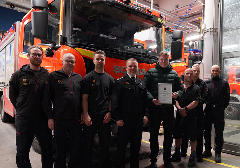 Palomiehet ja kunniakirjan saanut mies seisovat paloauton edessä