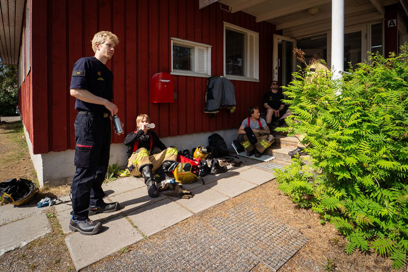 Firefighters drinking water from a bottle in the shade.