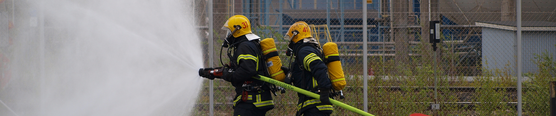 Kaksi pelastajaa harjoittelee tehdasalueella syttyneen palon sammuttamista.