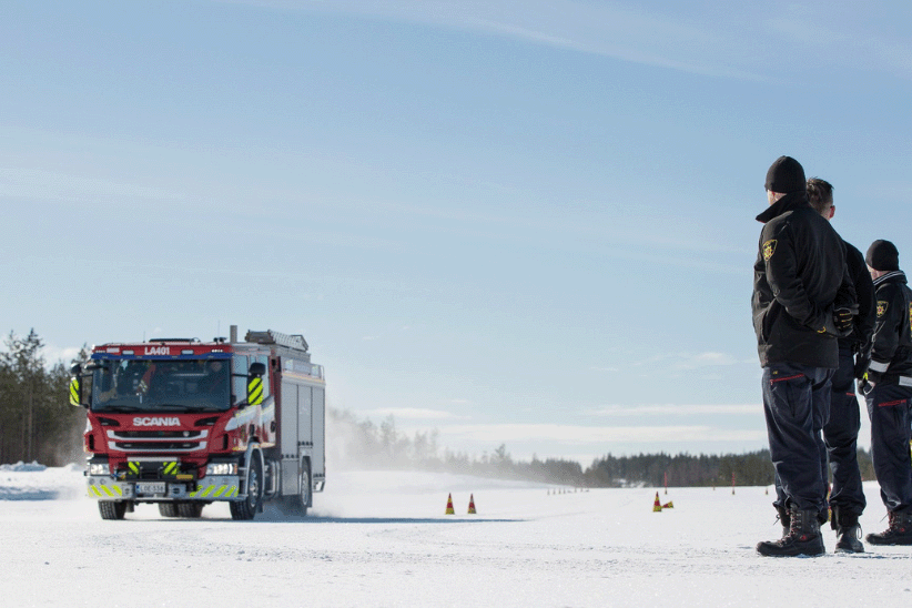 Pelastusajoneuvon ajoharjoitukset lumisella ajoradalla. Kolme pelastajaa seuraa ajoharjoitusta sivussa.