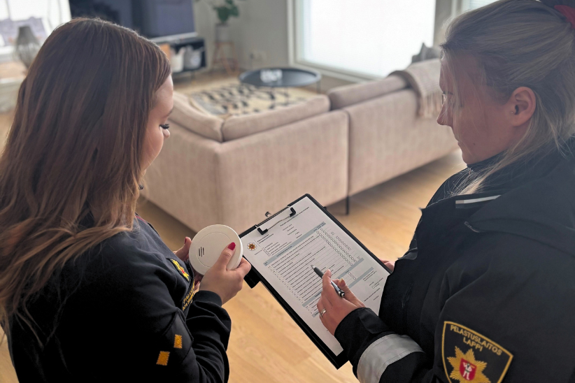 Kaksi palotarkastajaa tarkastelee palovaroitinta ja itsearviointilomaketta.