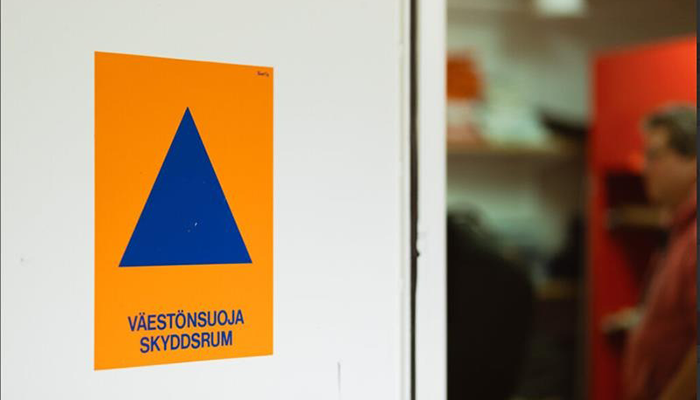 Väestönsuojelun ja väestönsuojan merkki: tummansininen kolmio oranssilla taustalla.