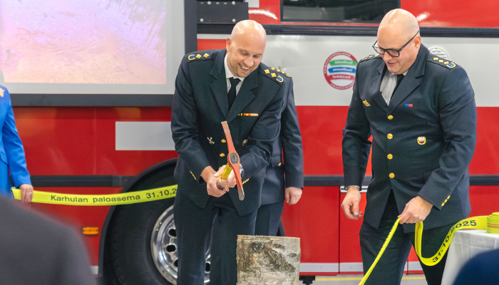 Pelastusjohtaja katkaisemassa paloletkua Karhulan paloaseman käyttöönottojuhlassa. Vieressä letkun katkaisua seuraa palopäällikkö.