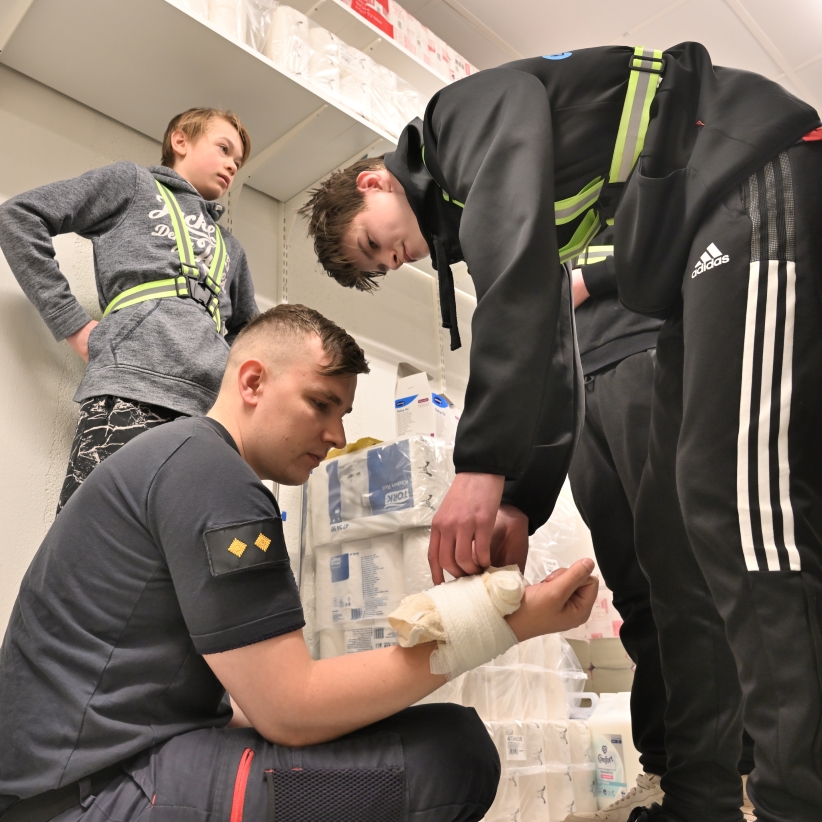 Nuori laittaa sidettä miehen käteen.