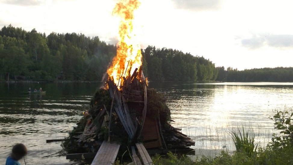 Kokko palaa kesäisen järven rannalla. Edessä lapsi.