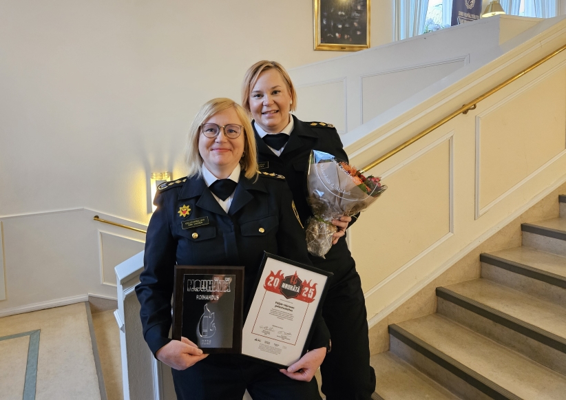 Kaksi iloista naista kunniakirja kädessä pelastusalan virka-asussa.