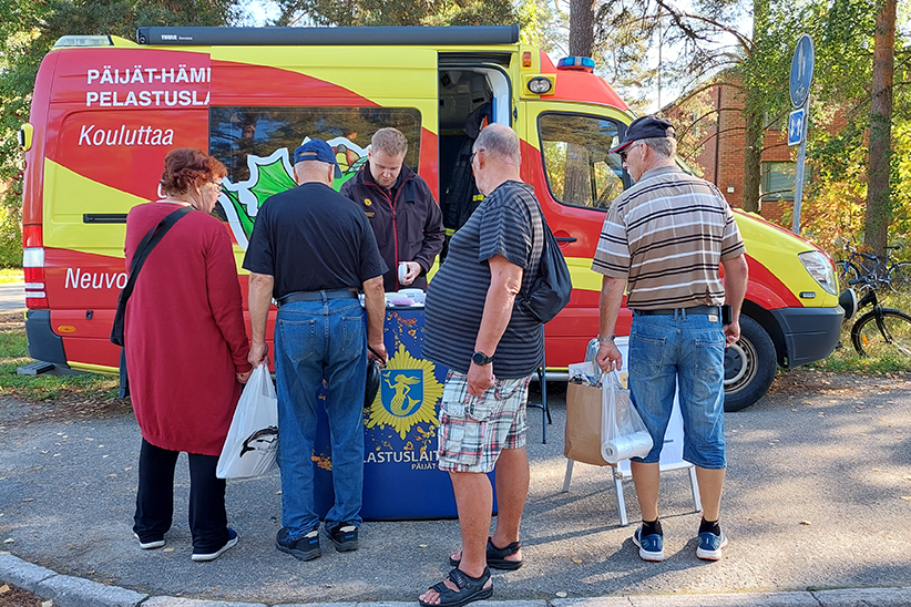 Ambulanssin näköinen pelastuslaitoksen koulutusauto, jonka edessä neuvontapiste, jossa ihmisiä kerääntyneenä.