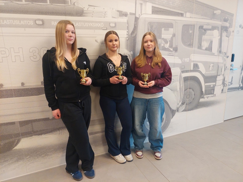 Kolme nuorta tyttöä pokaalit kädessä.