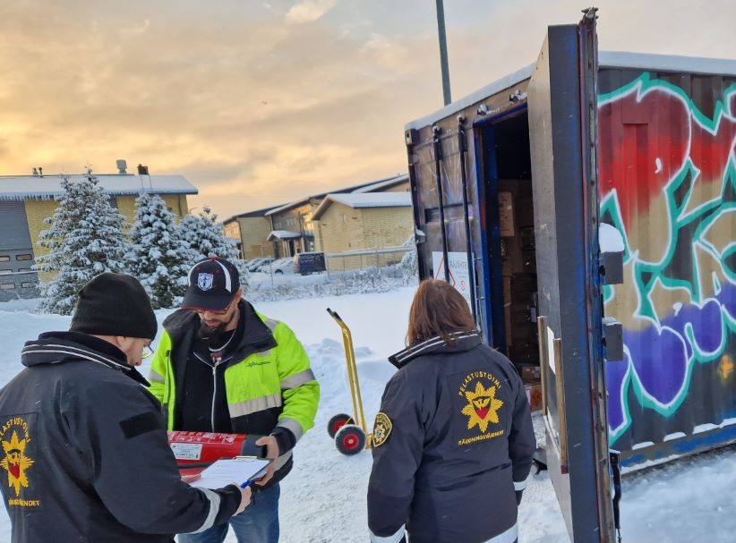 Pelastusviranomaisia ulkona kolmannen henkilön kanssa tarkastamassa konttia.