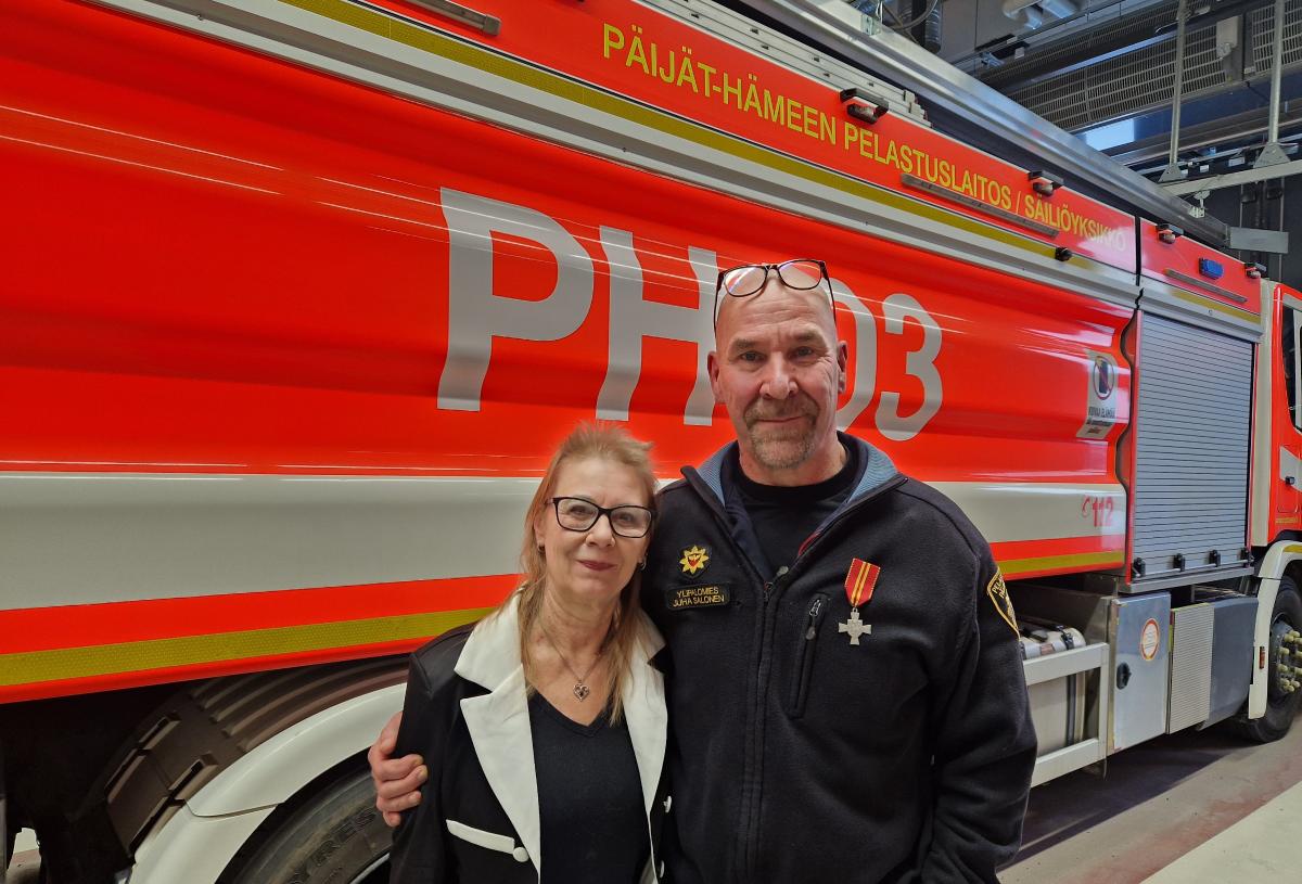 Paloauton edessä pelastusalan siniseen asuun pukeutunut mies ja siivilivaatteissa oleva nainen.