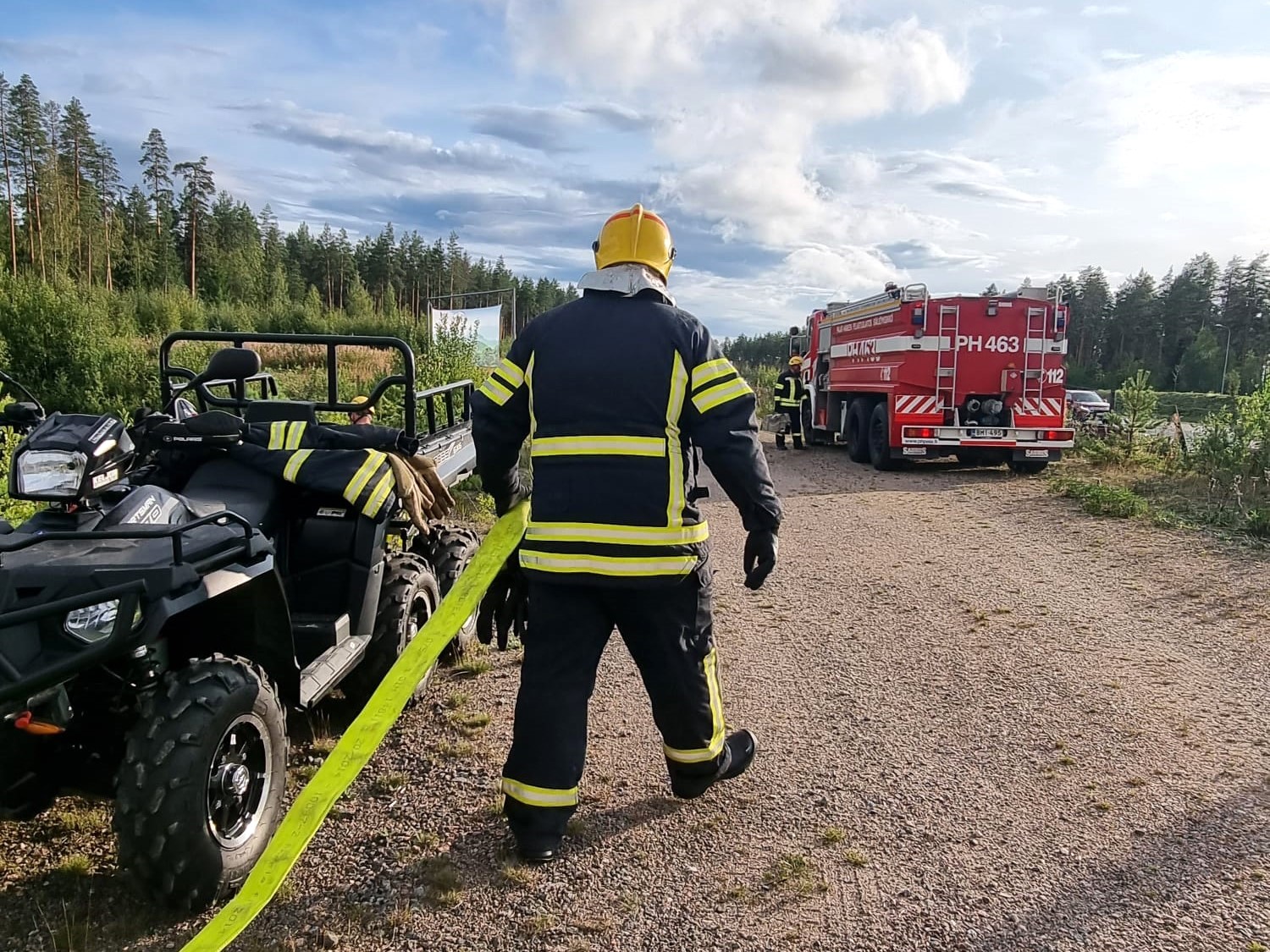 Pelastaja vetää paloletkua hiekkatiellä.
