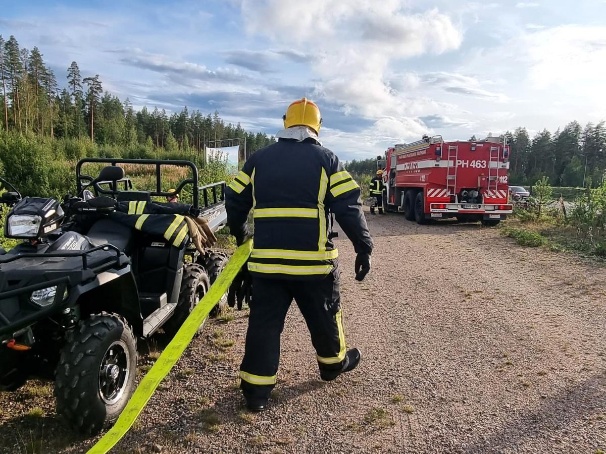 Pelastaja vetää paloletkua hiekkatiellä.