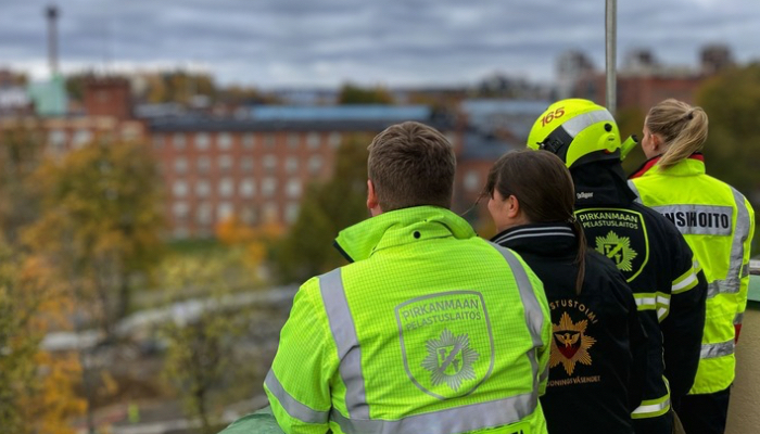  Pelastus- ja ensihoitopalveluiden henkilöstöä työtakeissaan Keskuspaloaseman letkutornissa syksyisessä maisemassa. 