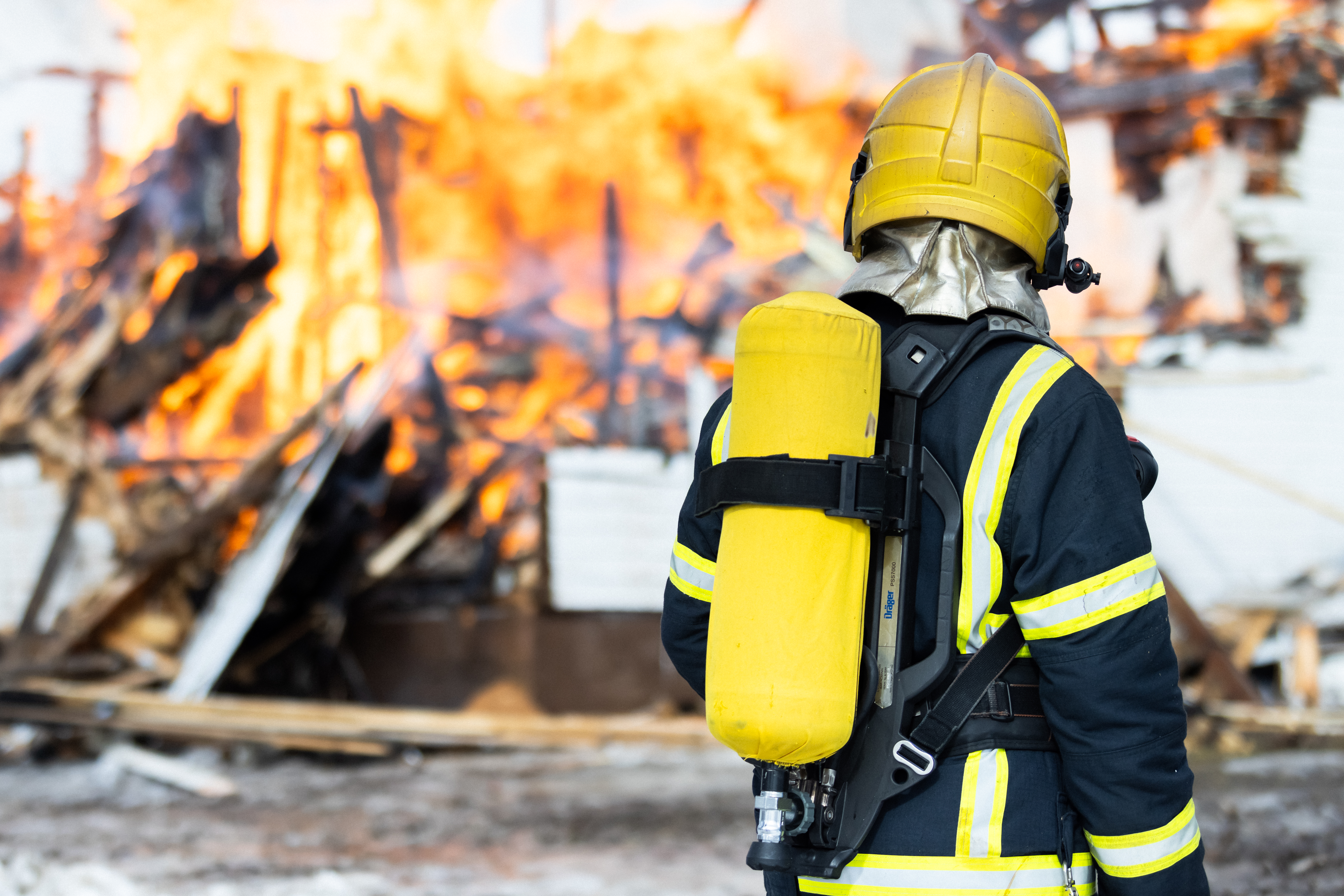  Pelastaja seisoo sammutusasu päällä palavan talon edessä. 