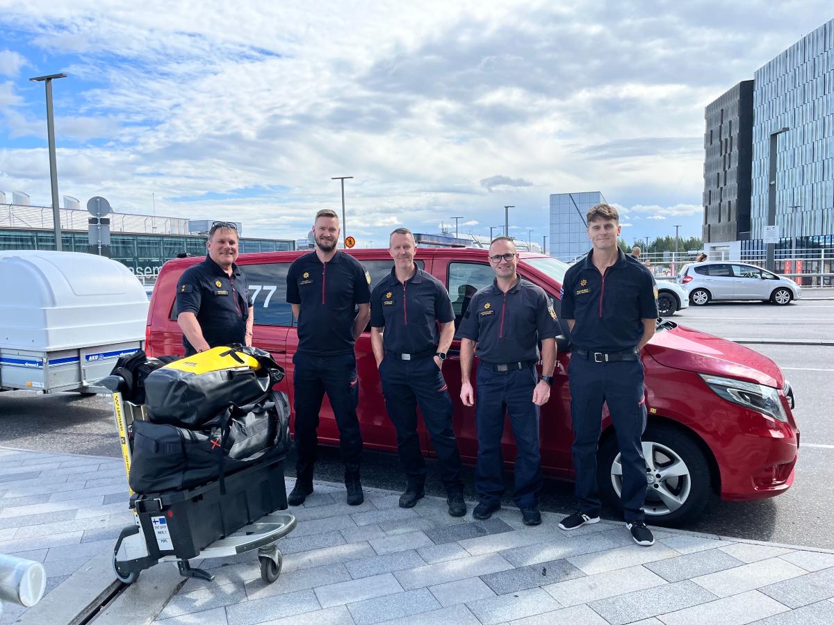 Viisi pelastajaa Pohjois-Savon pelastuslaitokselta seisovat rivissä lentokentällä.