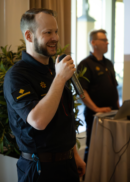 Riskienhallintapäällikkö puhuu mikrofoniin, takana seisoo palomestari.