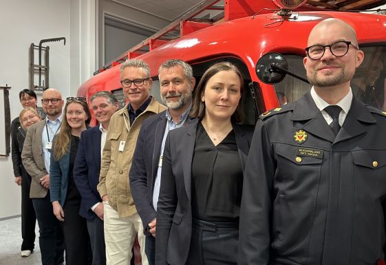 Pohjois-Savon pelastuslaitoksen valmiuspäällikkö seisoo kansainvälisten vieraiden kanssa paloauton edessä.