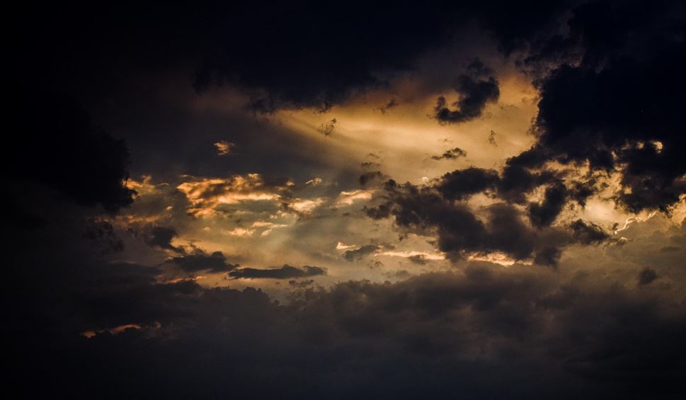 Taivaalla tummat myrskypilvet, joiden välistä näkyy vielä auringon säteitä.