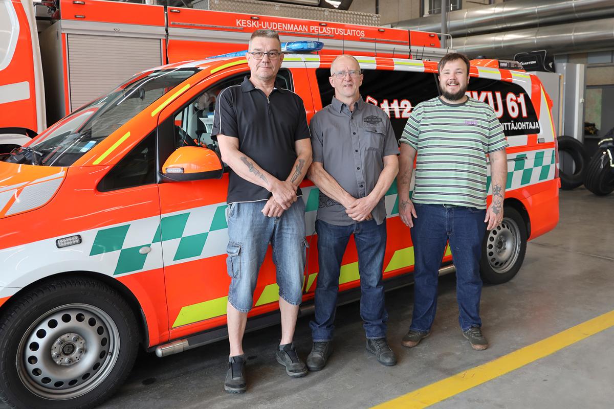 Kolme miestä seisoo ensihoidon kenttäjohtoyksikön edessä.