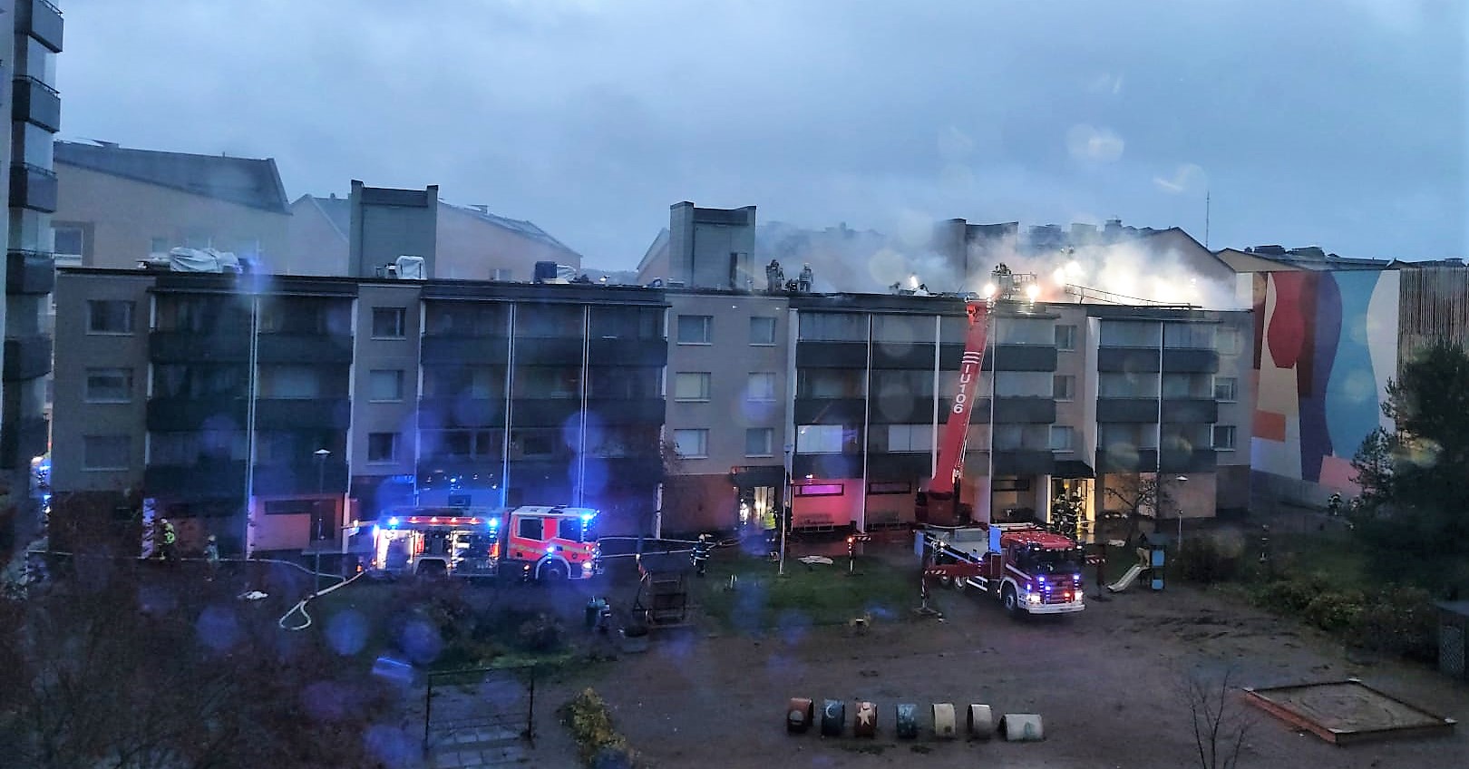 Paloautot sammuttavat kerrostalon kattoa, joka on tulessa.