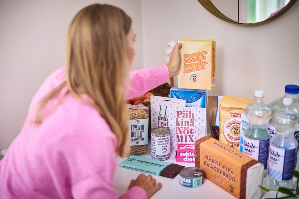 Nainen vaaleanpunainen paita päällä kasaa pöydälle kotivaraa.