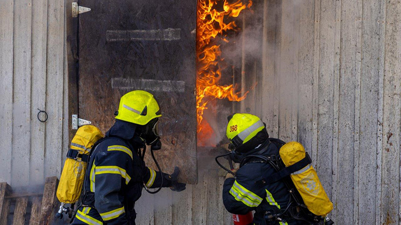 Kaksi pelastajaa sammuttaa rakennuksen tulipaloa sammutusvarusteet päällään.